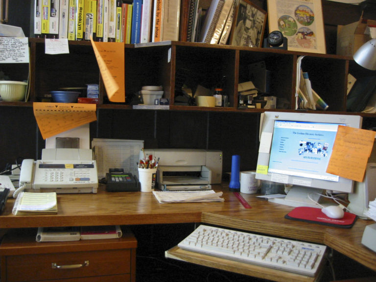 Workspace with an old computer on the desk, behind it are full shelves of books and objects